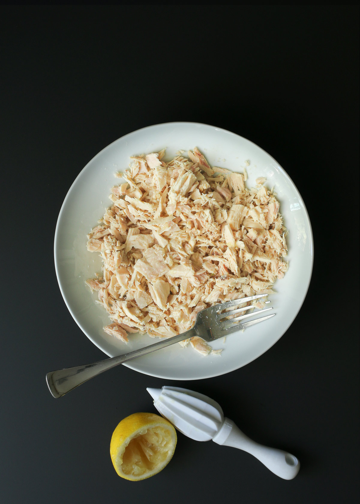 tuna fish flaked with a fork in a bowl, next to a lemon half and citrus reamer.