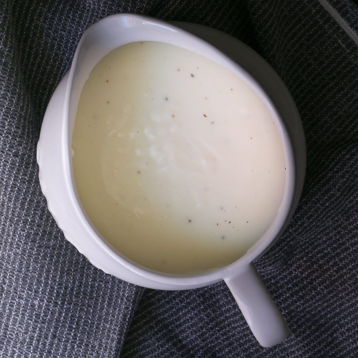 white sauce in white gravy boat on a gray cloth.