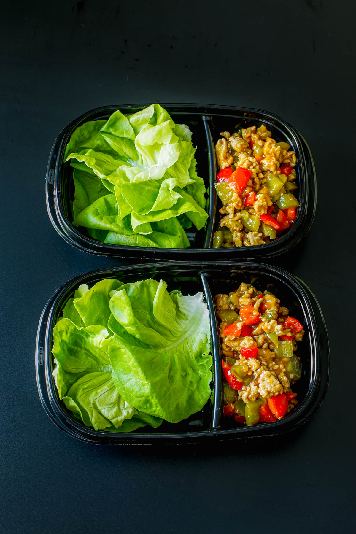 two divided meal prep boxes with lettuce leaves on one side and filling in the other.