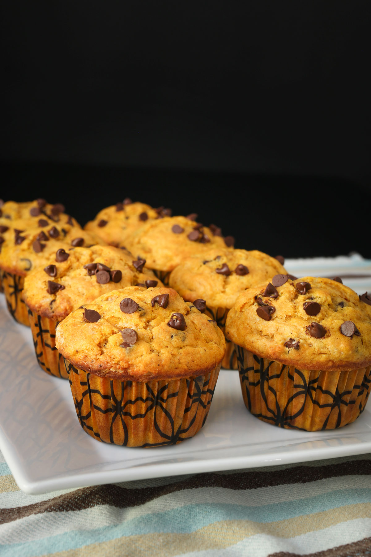 pumpkin muffins lined up on a white serving tray on a blue striped cloth.