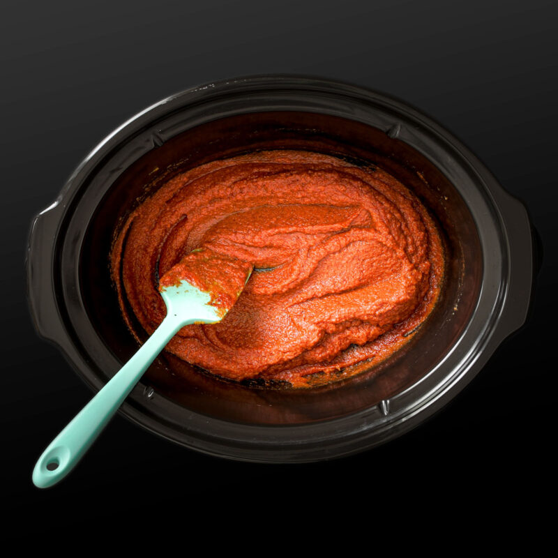 stirring together the pumpkin, tomato, and spices in the crock with a blue spatula.