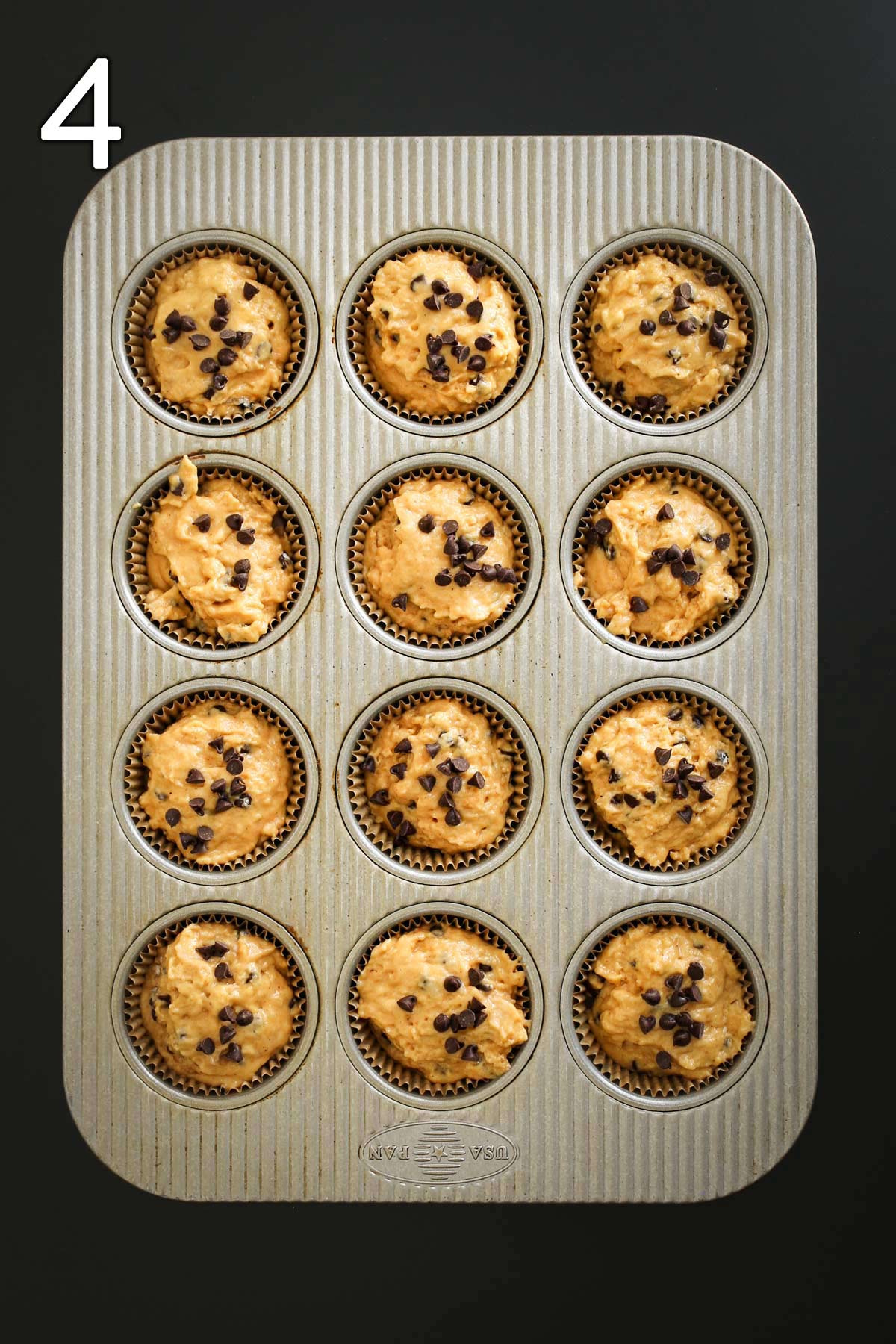 pumpkin muffin batter in tin topped with chocolate chips.