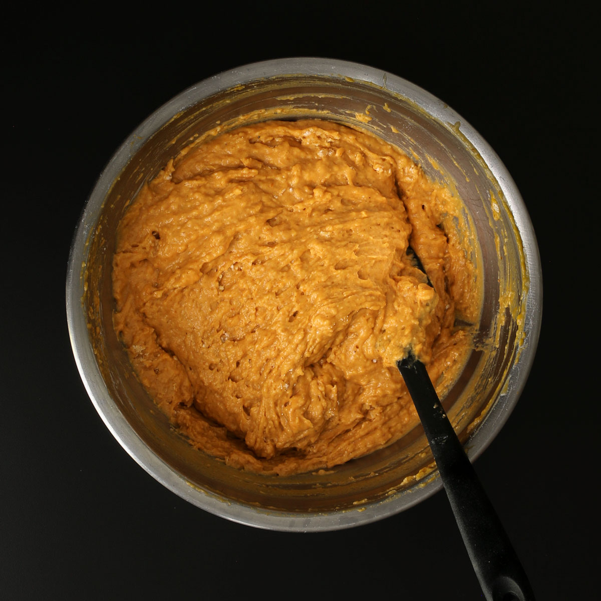 a black spatula immersed in the cake batter in the mixing bowl.