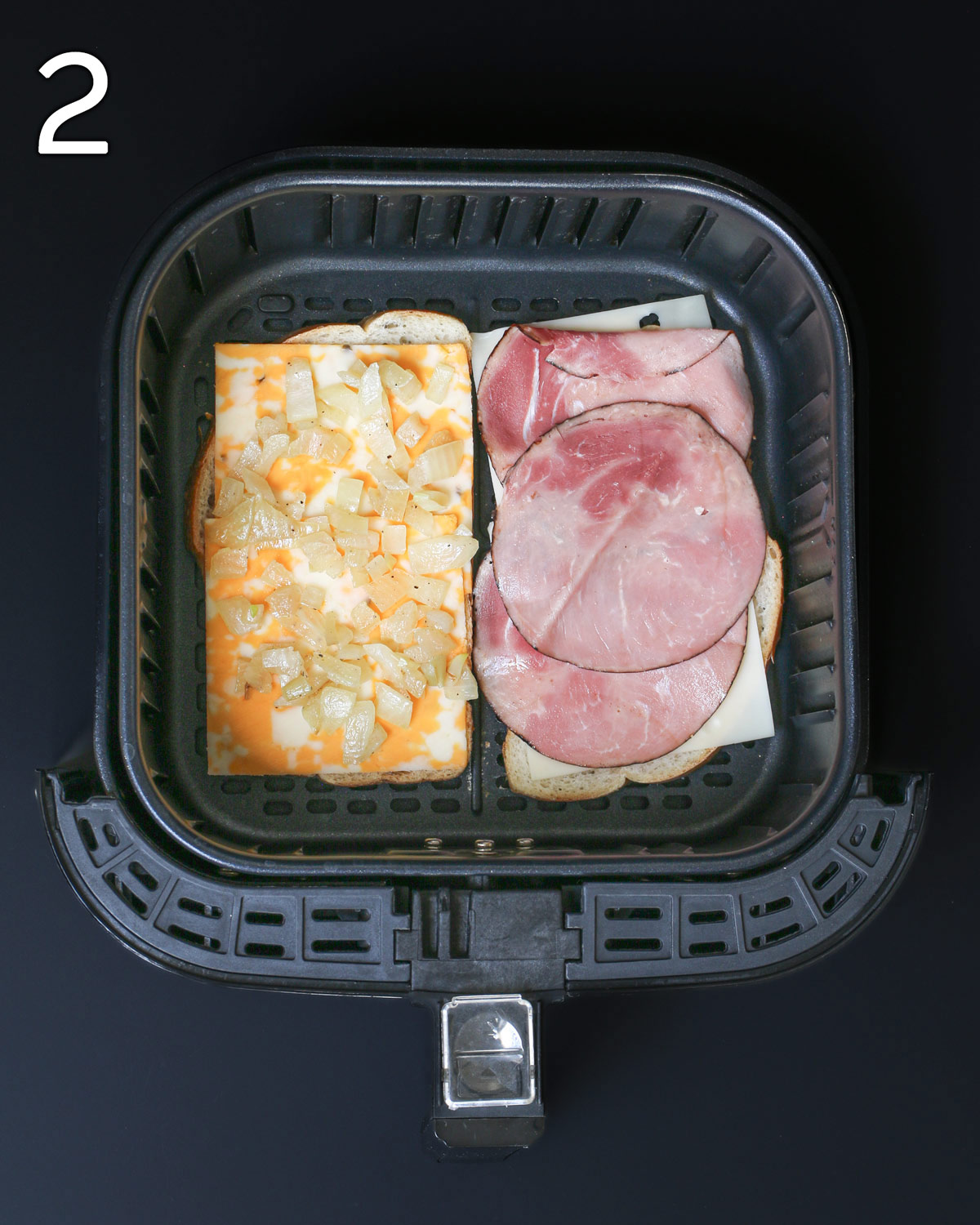 cheese and sandwich fillings layered on two slices of bread in air fryer.