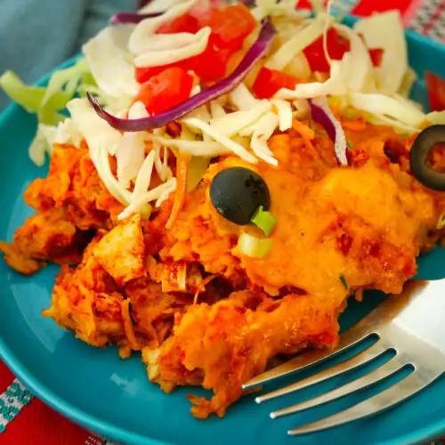 close up of crockpot enchiladas on a blue plate with fork and salad.
